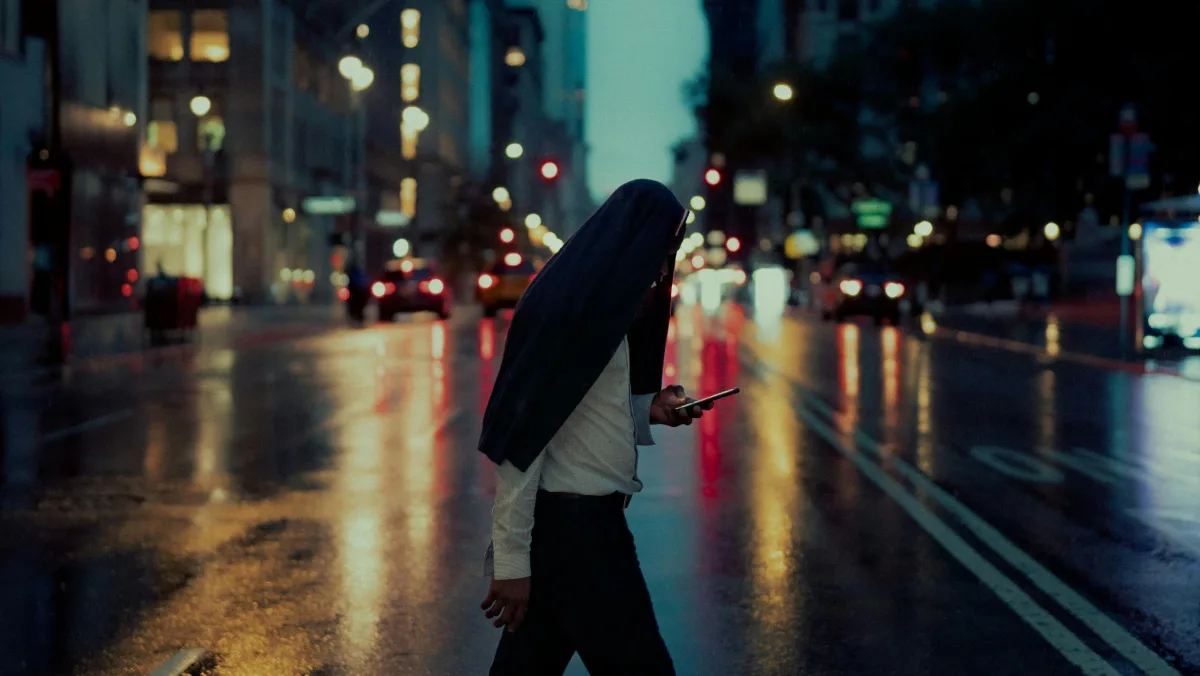 A person walking across a wet city street while holding a smartphone