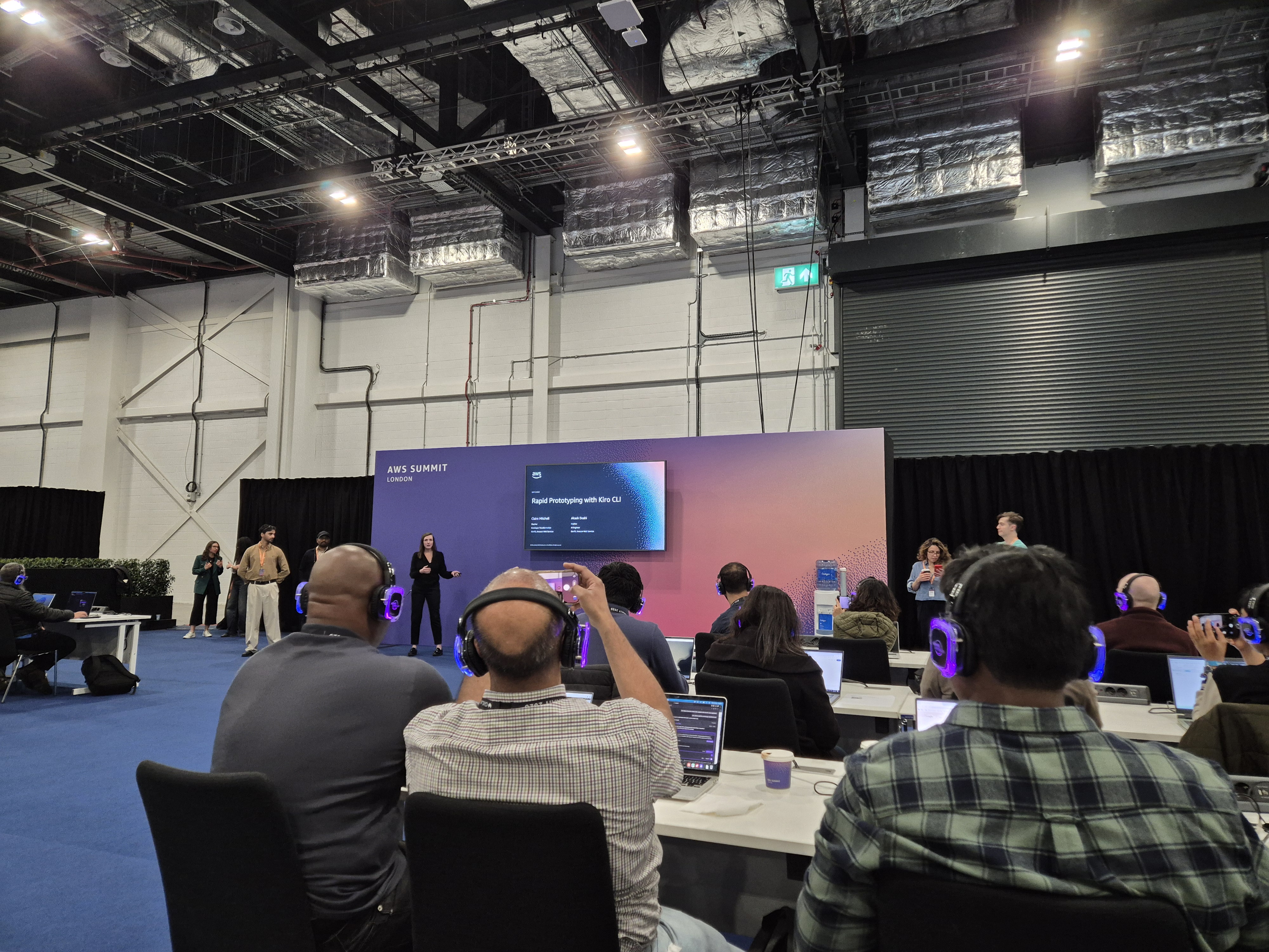 Attendees in the Kiro workshop at AWS Summit London 2026, seated with headphones while the presenters introduce the session