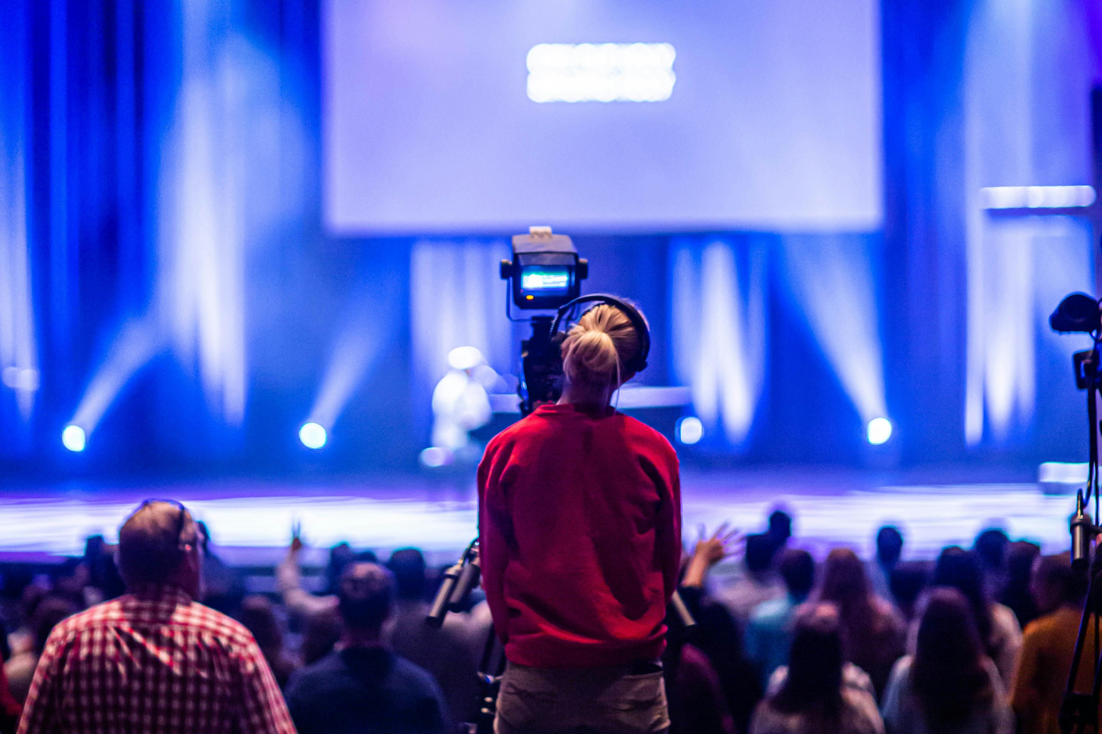 Conference stage with blue lighting and a cameraman filming
