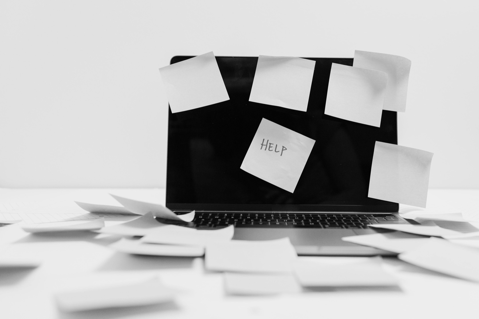 A laptop covered in blank sticky notes with one note saying help