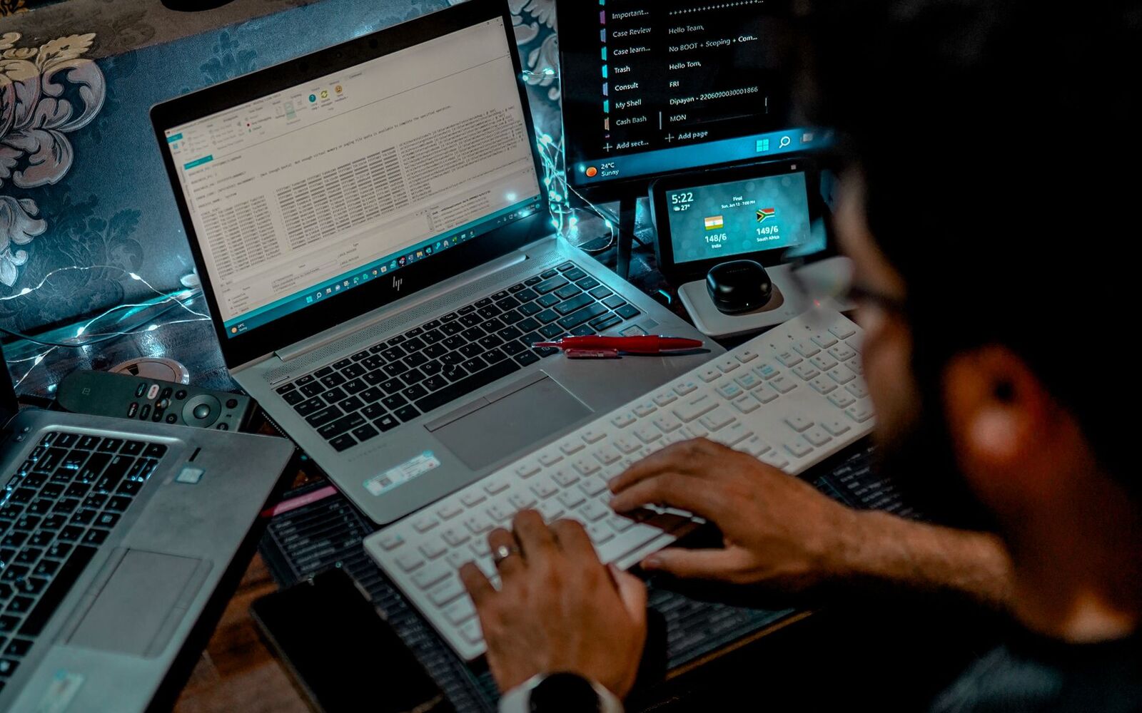 A person working across a laptop and multiple displays at a densely equipped desk